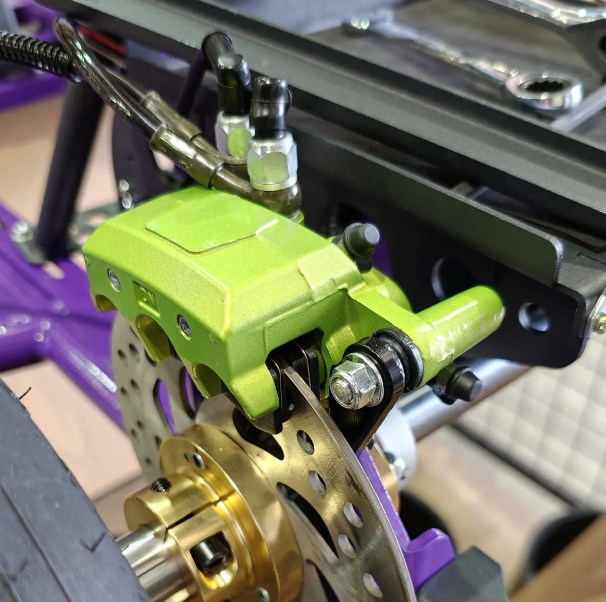 Close-up of the green opposed brake caliper on the drilled disc and gold hub of the live rear axle