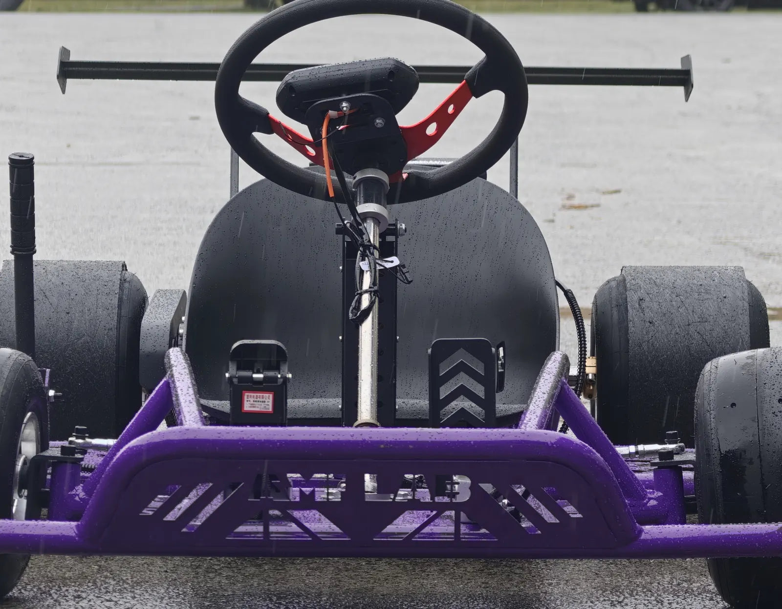Front view of the purple kart showing the full-width AMPLAB bumper, pedals, seat and rear wing